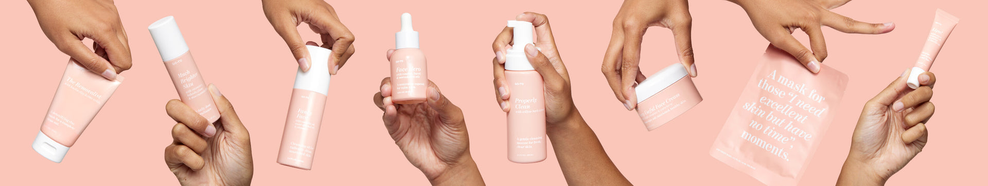 Hands holding various pink skincare products, including tubes, bottles, jars, a dropper, and a sheet mask, all displayed against a matching pink background.