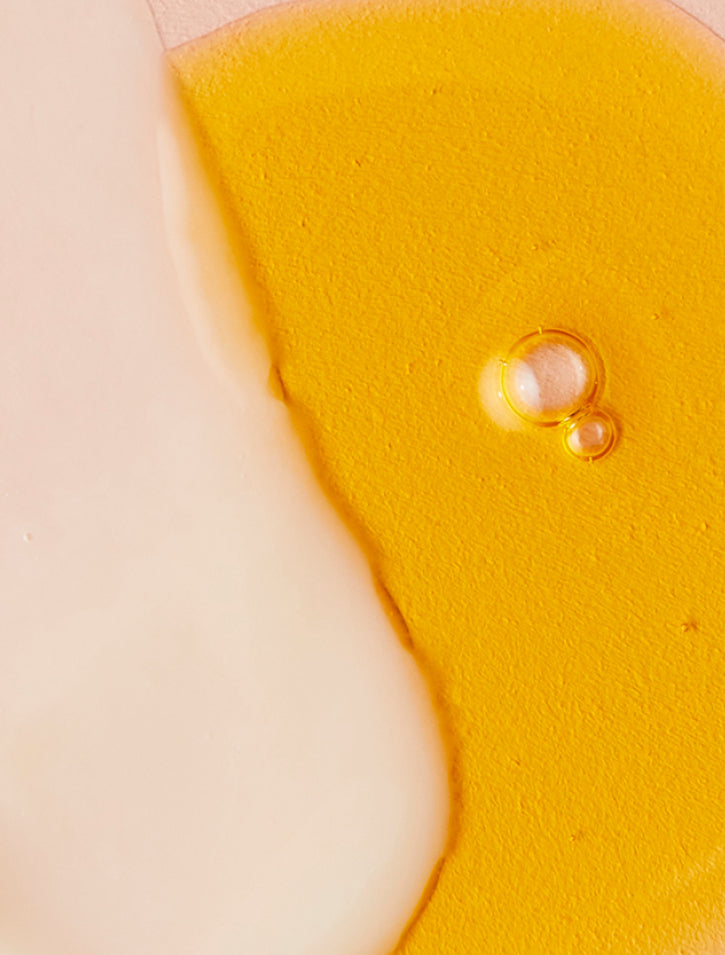 A close-up image of a creamy white liquid and golden yellow oil side by side, with a few small bubbles visible in the oil. The liquids have smooth, glossy textures and overlap slightly.