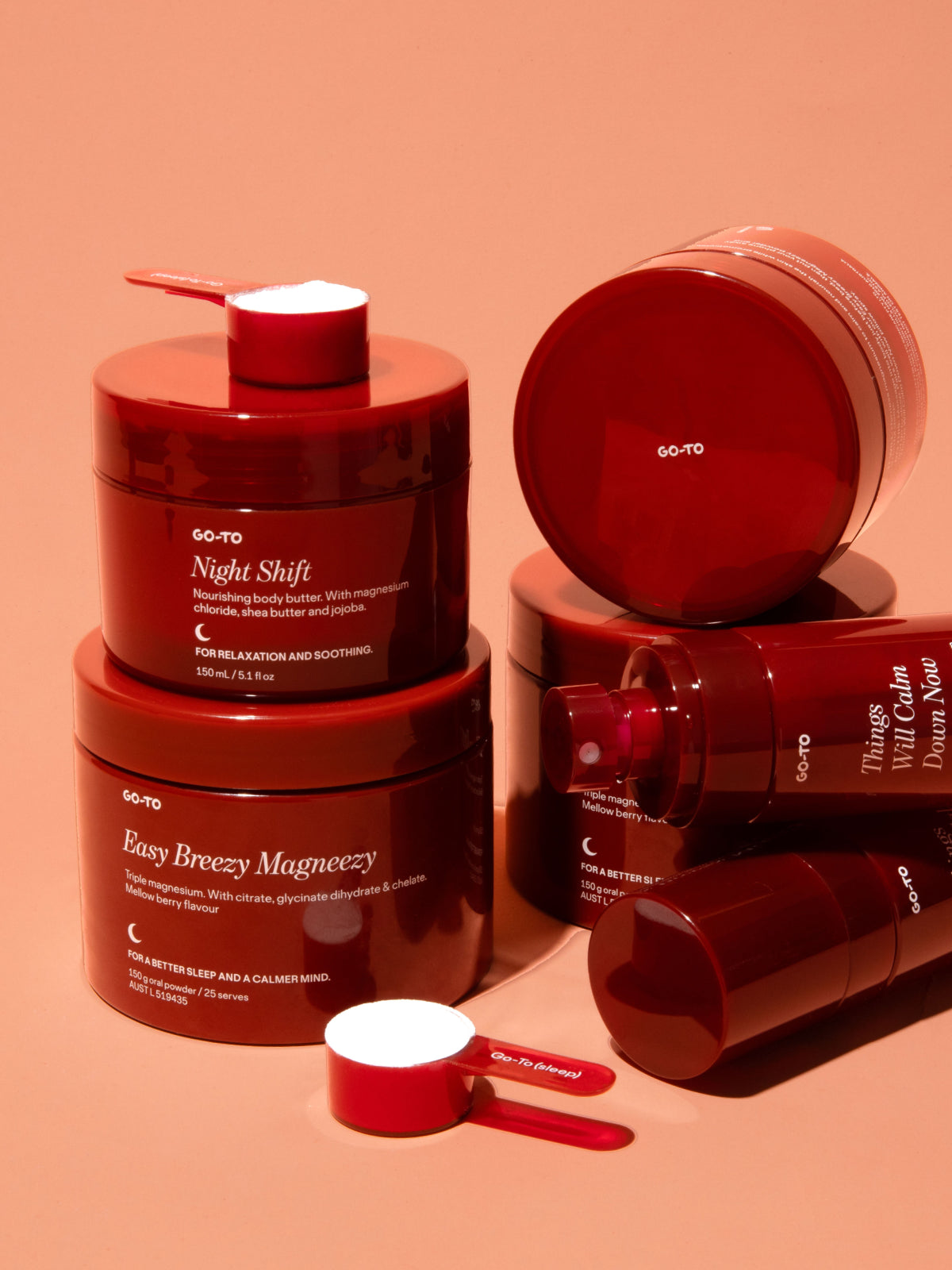Red jars of Go-To skincare products with scoops on a peach background, featuring Night Shift body butter and Easy Breezy Magneezy.
